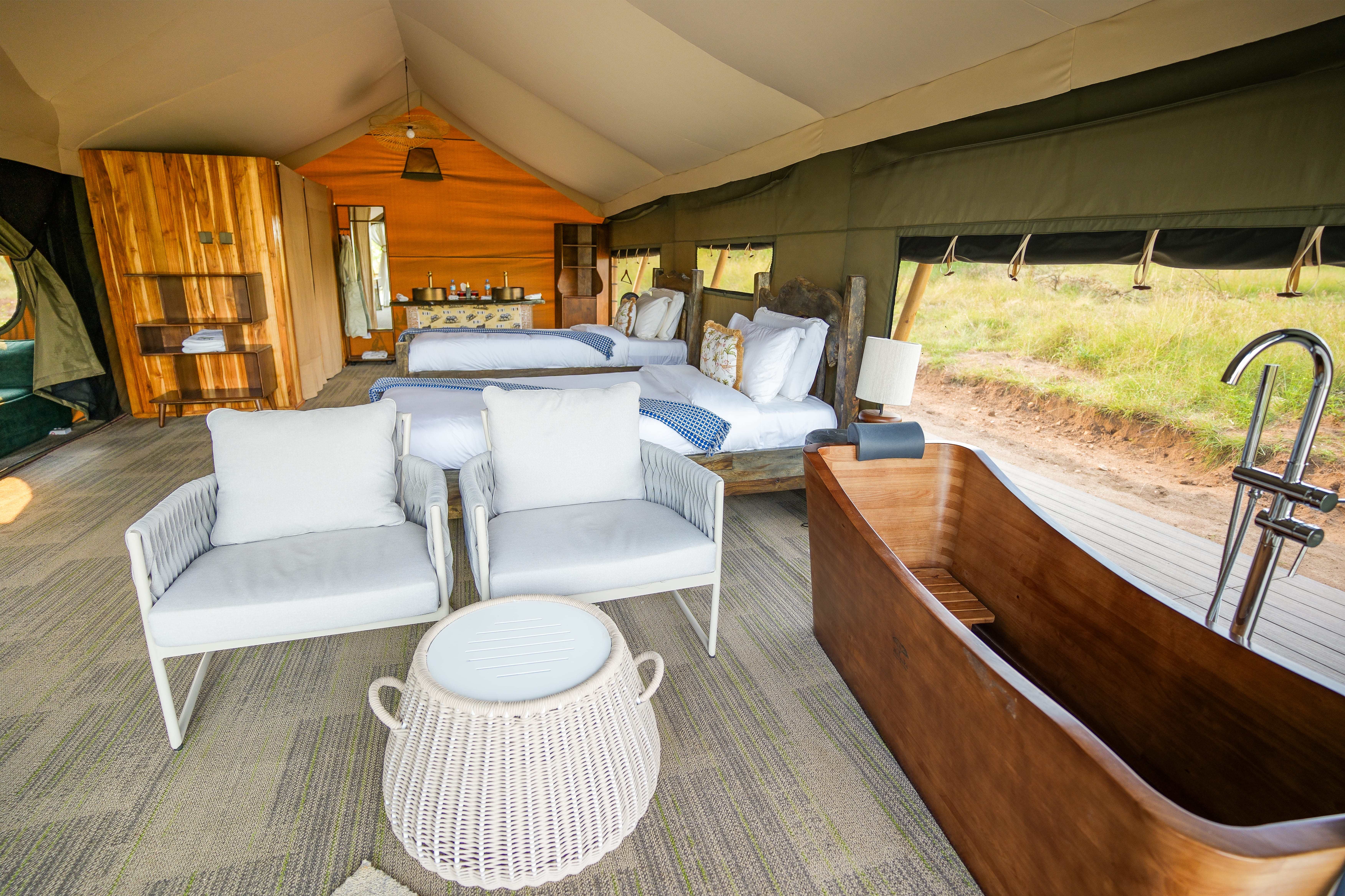 Spacious family tent interior with modern seating area, wooden bathtub, and panoramic savanna views