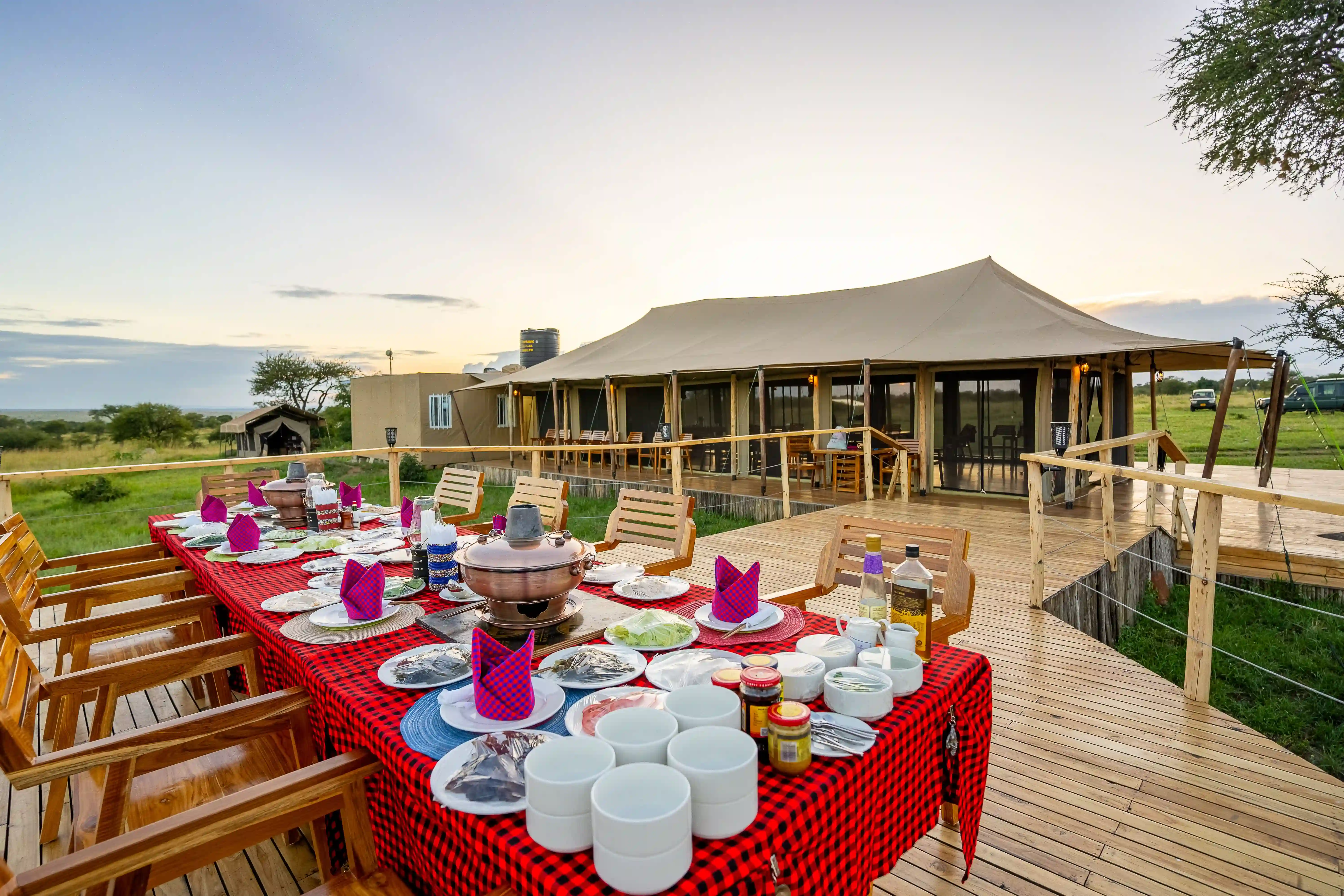 Outdoor dining setup on wooden deck with traditional Maasai-patterned tablecloth during golden hour