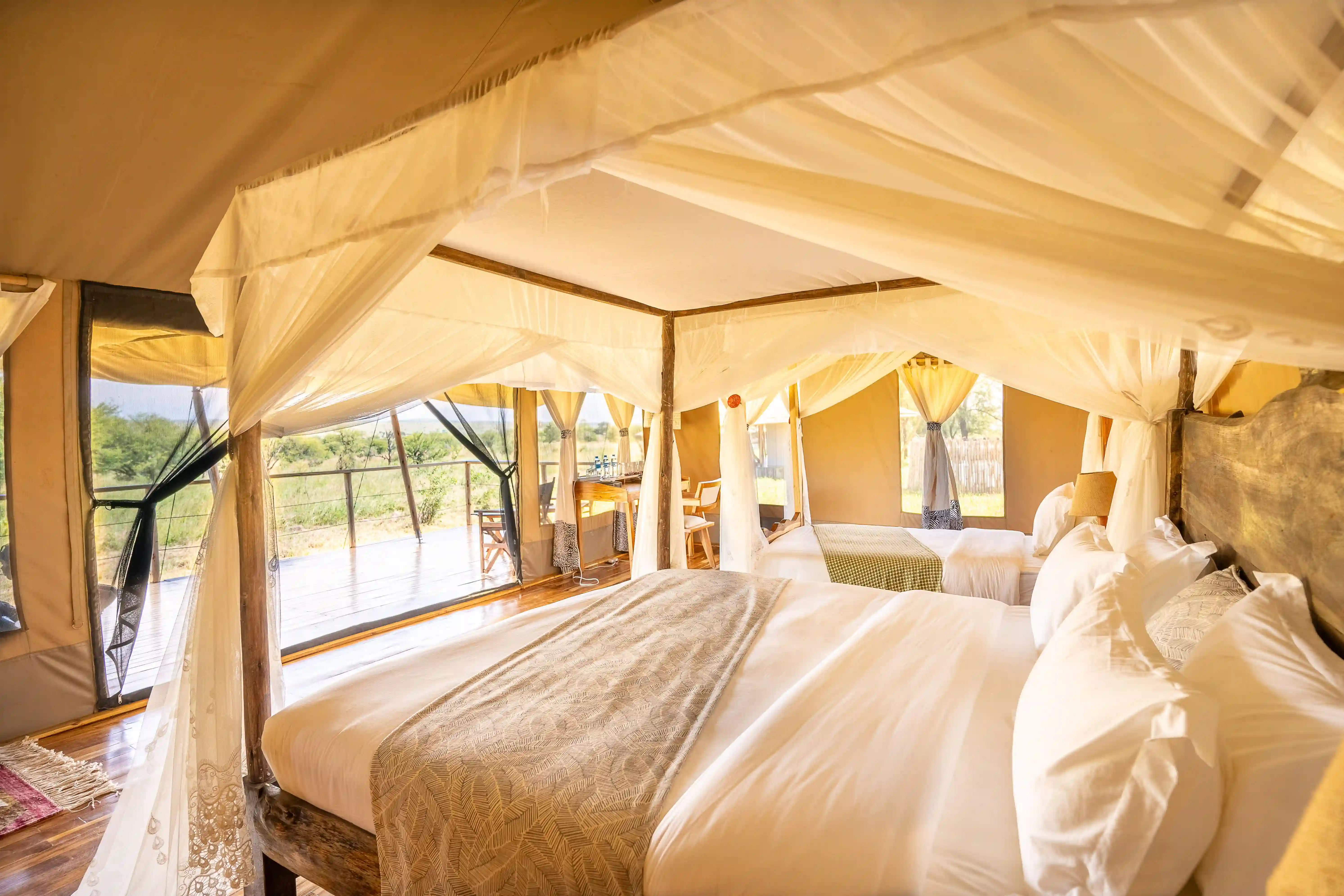 Romantic tent with flowing canopy beds, white curtains, and views to outdoor deck overlooking landscape